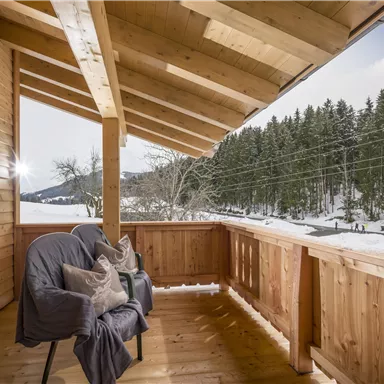 Ein gemütlicher Balkon aus Holz mit zwei Sesseln. Im Hintergrund sind schneebedeckte Landschaften und Nadelbäume zu sehen.