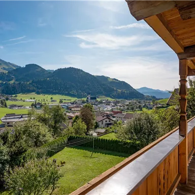 A picturesque view of a Bavarian village with green meadows and mountains in the background. The sky is clear and sunny.