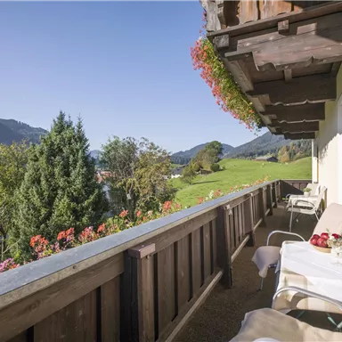 A beautiful balcony with a view of green meadows and mountains. The flowers and furniture invite you to relax.