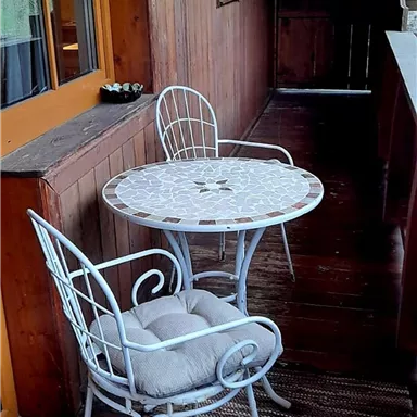 A small balcony with a round table and two white chairs. The wooden cladding and the floor create a cozy atmosphere.