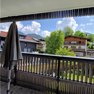 A balcony overlooking green trees and a lovely residential area. The sky is clear with some clouds.