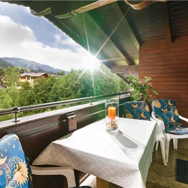 A beautiful balcony with a table and two chairs. In the background, the mountains and nature are clearly visible.