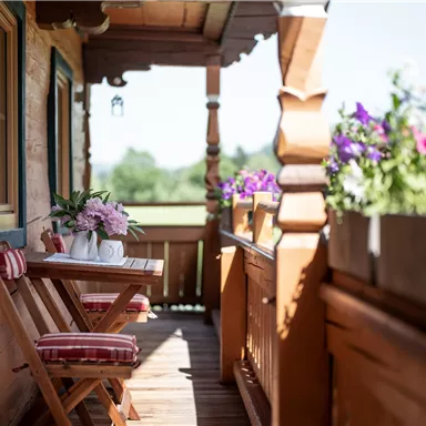 Ein einladender Balkon mit einem Holztisch und bunten Blumen. Die sonnige Aussicht lädt zum Entspannen ein.