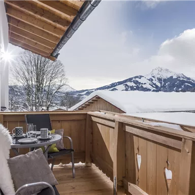 A cozy balcony with a view of snow-covered mountains. Glasses and decorations are on the table in a tranquil winter landscape.