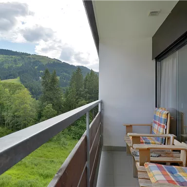 A balcony with two comfortable chairs and a magnificent view of a green landscape. In the background, hills and trees can be seen.