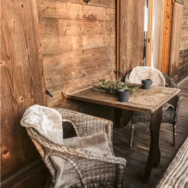 Ein rustikaler Sitzbereich mit zwei Stühlen und einem Tisch. Die Wand ist aus Holz und es sind dekorative Elemente sichtbar.