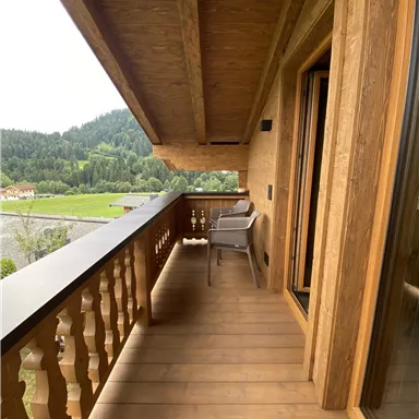A balcony with wooden cladding and a view of the mountain landscape. There is a chair on it, and the atmosphere is calm and inviting.