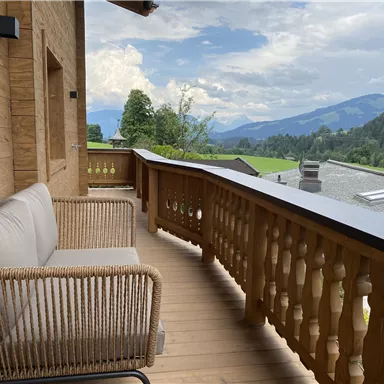 A cozy balcony with a rattan sofa and a view of green mountains. The atmosphere is relaxed and inviting.