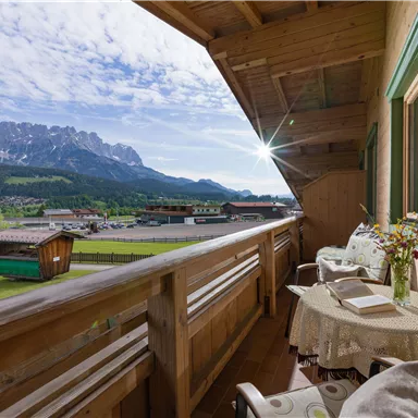 A balcony overlooking mountains and a green valley. A table and two chairs invite you to relax.