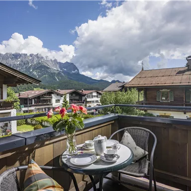 Ein gemütlicher Balkon mit Blick auf die Berge. Ein Tisch mit einer Teekanne und frischen Blumen lädt zum Entspannen ein.