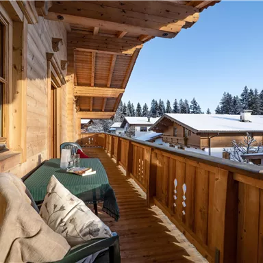 Ein Holzbalcony mit einem Tisch und Stühlen. Die Umgebung ist schneebedeckt und von Bäumen umgeben.