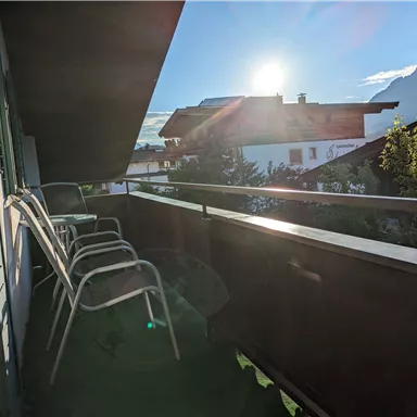 Ein Balkon mit mehreren Stühlen und Blick auf die Berge. Die Sonne scheint hell und der Himmel ist klar.