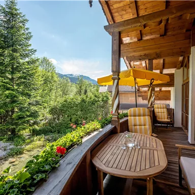 A beautiful balcony with a wooden ceiling and comfortable seating. The view overlooks lush trees and green landscape.