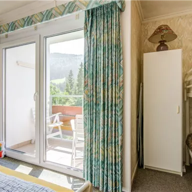 A bright room with a balcony view of the mountains. There is a bunk bed, a wardrobe, and a cozy armchair.