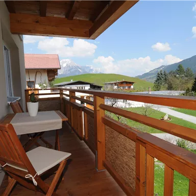 Ein schöner Balkon mit Holzgeländer und Blick auf die Berge. Ein Tisch und ein Stuhl laden zum Entspannen ein.