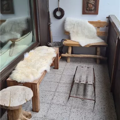 A cozy balcony with wooden furniture and furs. A picture and a decoration hang on the wall.