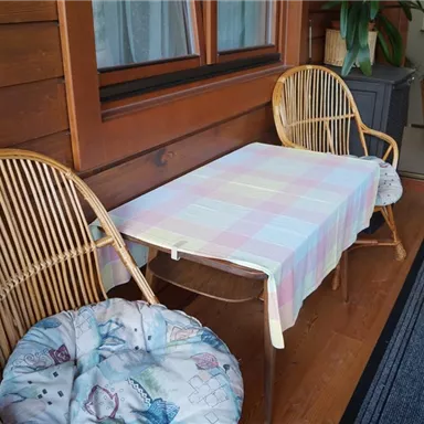 Ein gemütlicher Balkon mit zwei Korbstühlen und einem bunten Tisch. Der Tisch ist mit einer Decke bedeckt und der Boden ist mit einem Teppich ausgelegt.
