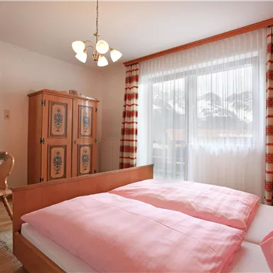 Ein gemütliches Schlafzimmer mit zwei Betten, die mit rosa Bettwäsche bezogen sind. Helle Vorhänge und eine Holzkommode verleihen dem Raum eine einladende Atmosphäre.