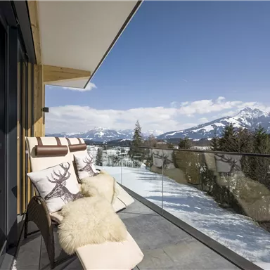 A modern balcony with comfortable lounge chairs and a beautiful view of the snow-capped mountains. The clear blue sky adds a relaxing atmosphere.