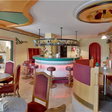 Eine gemütliche Bar mit roten Sitzen und einem halbkreisförmigen Tresen. Die Wände sind in warmen Farben gestaltet und es gibt angenehmes Licht.