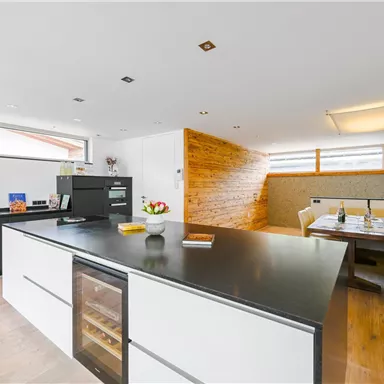 Eine moderne Küche mit einer großen Kochinsel und einem stilvollen Essbereich. Der Raum ist hell und freundlich, mit Holz- und Steinakzenten.