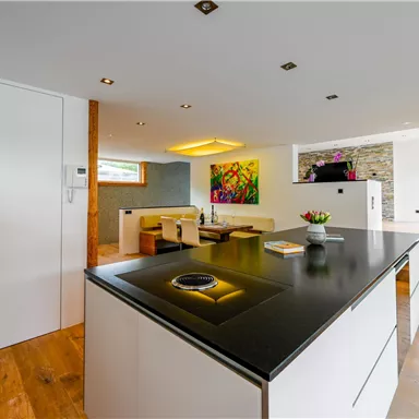 Moderne Küche mit elegantem, schwarzem Arbeitsbereich und Holzfußboden. Helle Räume mit Tageslicht und minimalistischer Einrichtung.