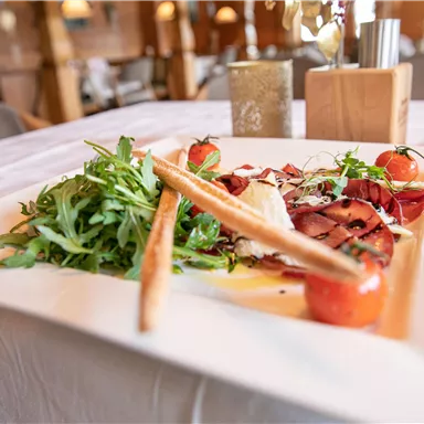 An appealingly arranged plate with salad, tomatoes, and ham. Accompanied by grissini and fresh herbs for decoration.