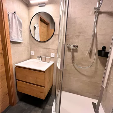 A modern bathroom with a shower and a wooden sink. On the wall, there is a round mirror.