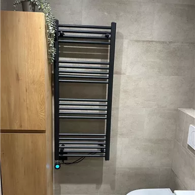 Ein modernes Badezimmer mit einem Handtuchwärmer an der Wand. Neben dem Handtuchwärmer steht ein Schrank aus Holz.