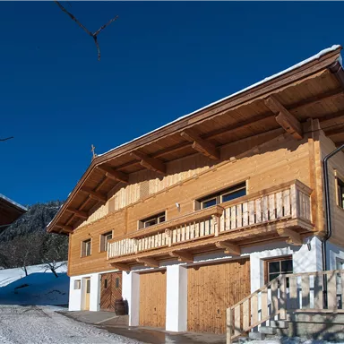 A wooden house in the snow with a clear blue sky. The architecture is traditional and cozy.