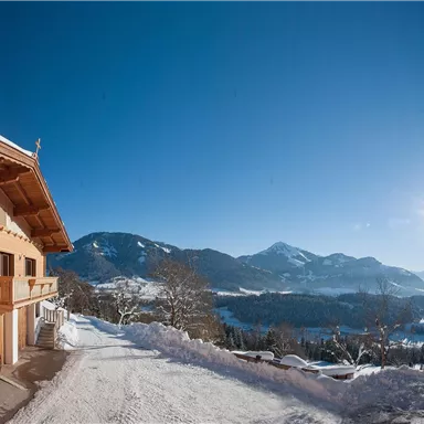 A chalet in the mountains, surrounded by snow and trees. The clear sky and sunny view create a beautiful, wintry atmosphere.