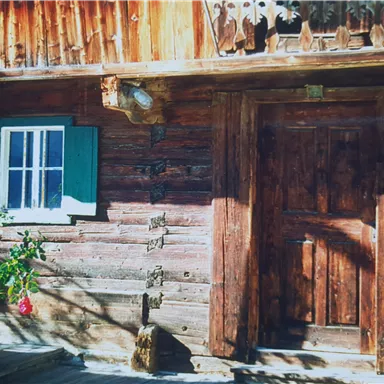 A rustic log cabin with a wooden door and a small window. Rose petals climb up the wall.
