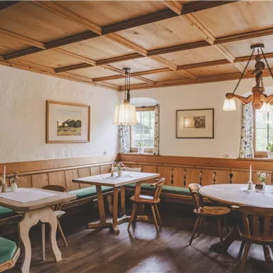 Ein gemütlicher Raum mit Holzvertäfelungen und Tischen. Die Dekoration ist einfach und einladend, mit Fenstern, die auf eine grüne Umgebung blicken.