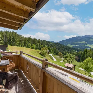 Ein schöner Balkon mit Holzverkleidung und Blick auf grüne Berge. Der Himmel ist blau mit einigen Wolken.