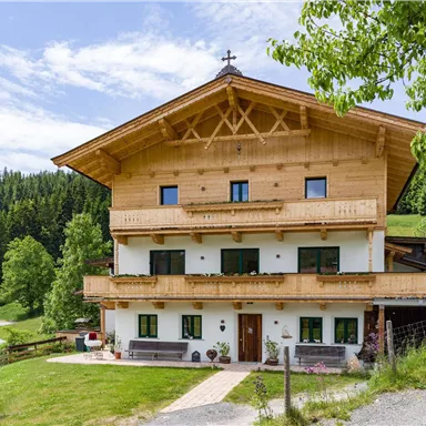 Ein traditionelles Holzhaus in den Bergen, umgeben von grünen Wäldern. Der klare Himmel und die schöne Landschaft schaffen eine idyllische Atmosphäre.