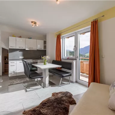 Ein modernes Wohnzimmer mit einer hellen Küche und Essbereich. Große Fenster bieten einen Blick auf die Berge.