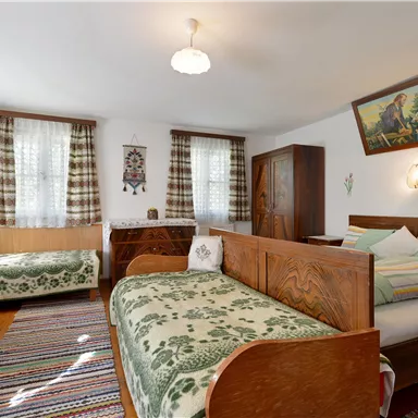 A cozy room with two beds, a wooden table, and chairs. The decor is rustic with colorful carpets and curtains.