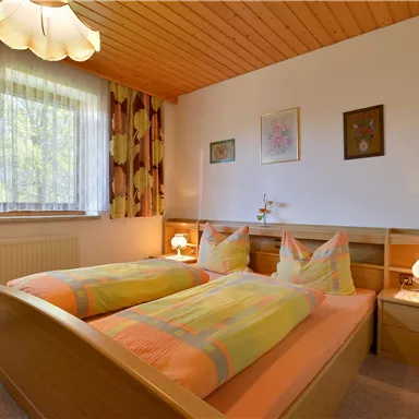A cozy bedroom with two single beds and colorful bedspreads. Large windows provide plenty of daylight and a friendly atmosphere.