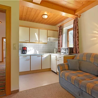 A cozy kitchen corner with modern kitchen cabinets and a sofa. The warm colors and wood ceiling design create an inviting atmosphere.