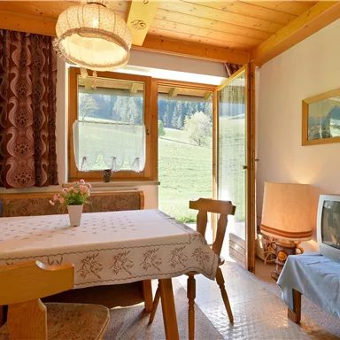 A cozy room with a table and chairs. There is a window overlooking the landscape and a television corner.