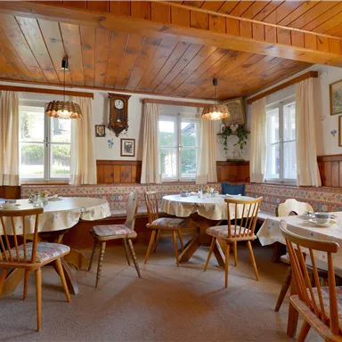 A cozy restaurant with wooden paneling and tables inviting you to sit down. Windows provide daylight and a warm atmosphere.