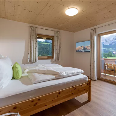 Ein gemütliches Schlafzimmer mit Holzschränken und einem großen Fenster. Der Blick zeigt die Berge und einen Balkon mit einem schönen Ausblick.