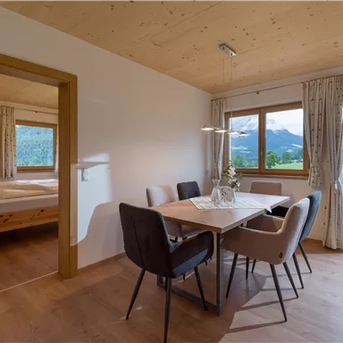 Ein gemütlicher Essbereich mit einem Tisch und Stühlen. Die große Fensterfront bietet einen Blick auf die Berge und die Natur.