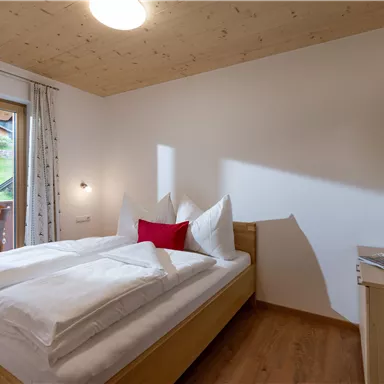 Ein gemütliches Schlafzimmer mit einem Doppelbett und weißen Bettdecken. Der Raum hat große Fenster, die auf einen Balkon mit Blick auf die Landschaft führen.