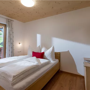 A cozy bedroom with a double bed and bright, modern furniture. Large windows provide a view of the nature outside.