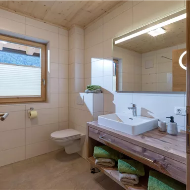 A modern bathroom with a wooden vanity and large mirror. There are bright tiles and pleasant lighting.