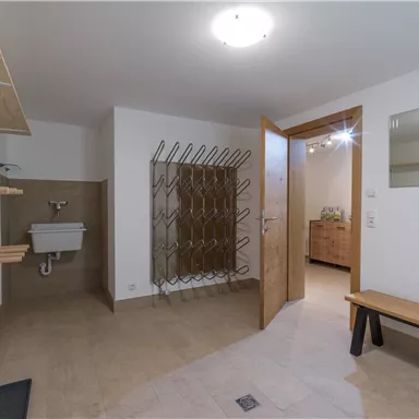 A bright room with a wooden bench and a mirror. On the wall are shelves and a coat rack with space for jackets and bags.