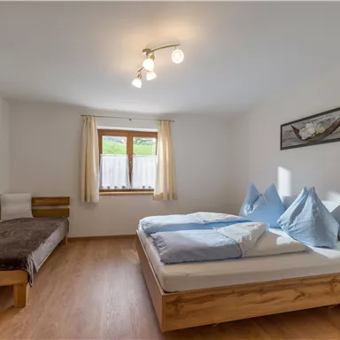 A cozy bedroom with two beds and an additional sleeping space. Large windows provide bright light and an inviting atmosphere.