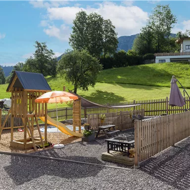 A beautiful playground with a slide and a sunshade. In the background, you can see a green meadow and houses.