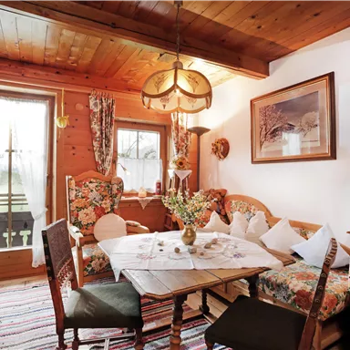 A cozy dining area with a round table and floral furniture. Large windows let in plenty of light and create an inviting atmosphere.